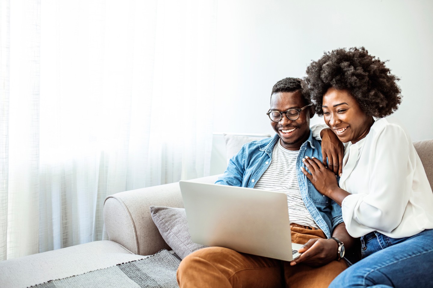 Happy African American couple sitting on couch and using a laptop