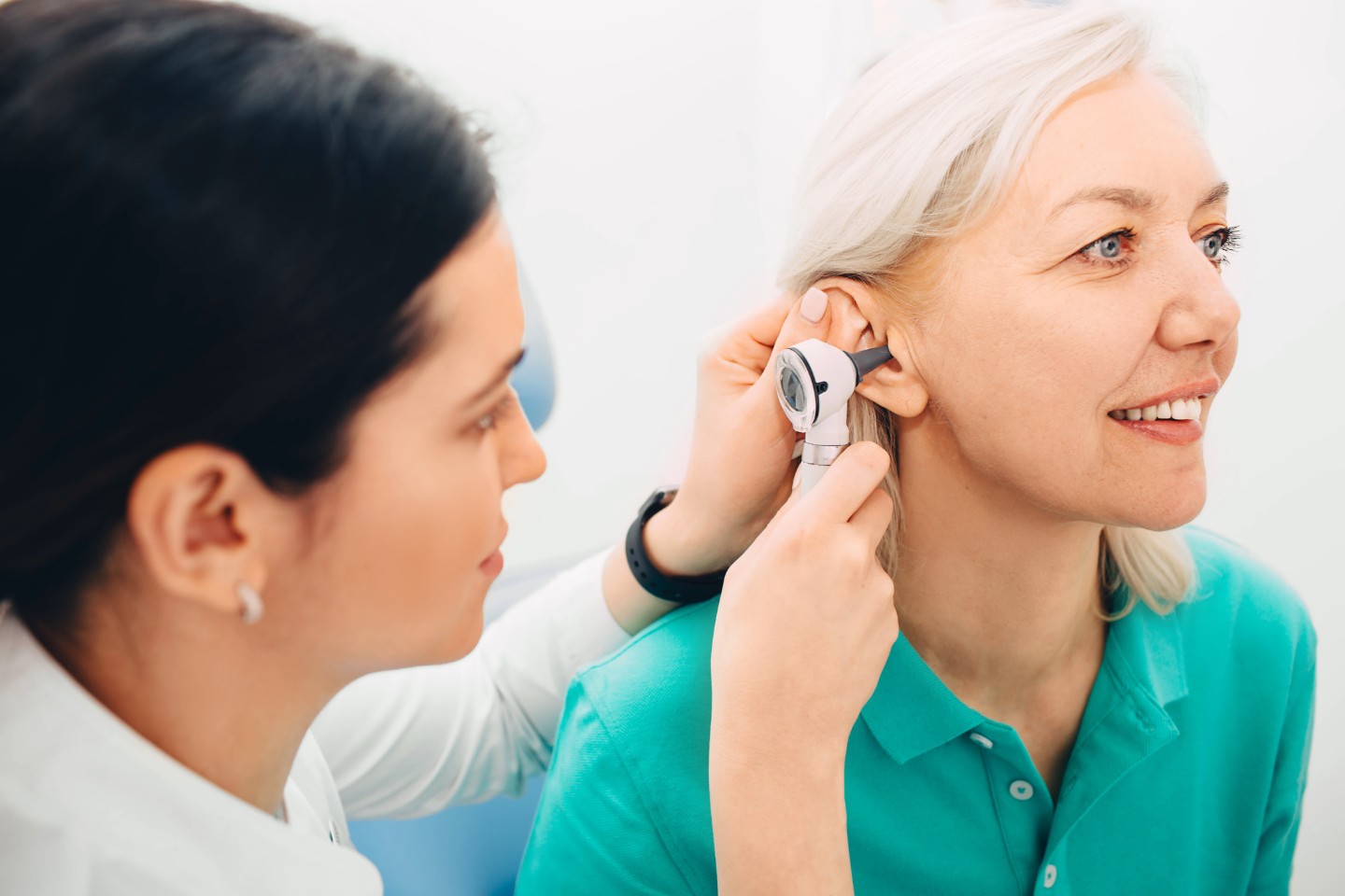 Mature woman getting ear exam at clinic, doctor examining patient ear, using otoscope