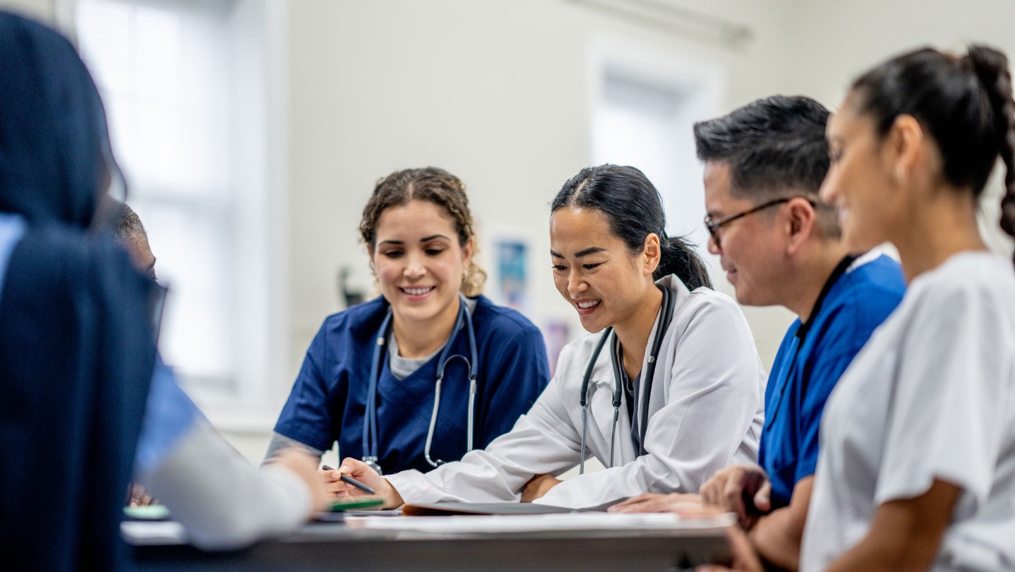 Woman in scrubs raising hand in classroom setting