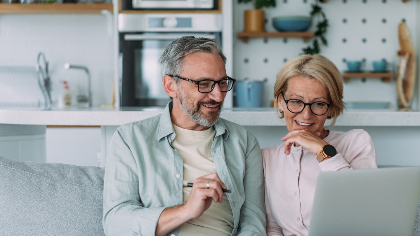 older couple smiling and sitting on the couch with a laptop