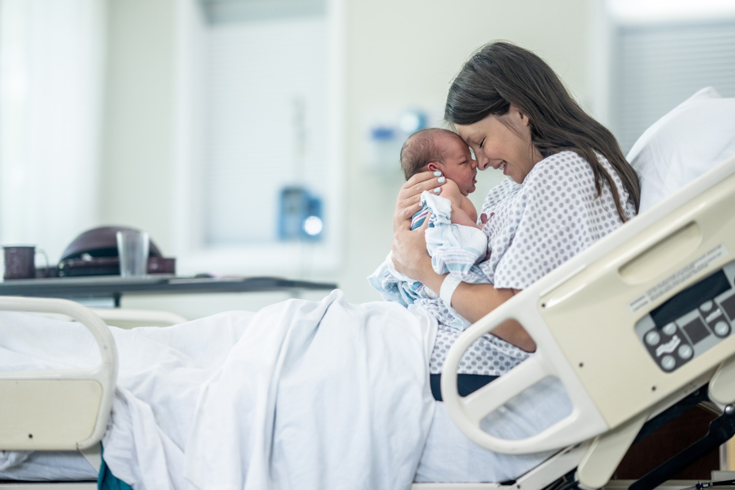 Mom smiling and holding her newborn in a hospital bed