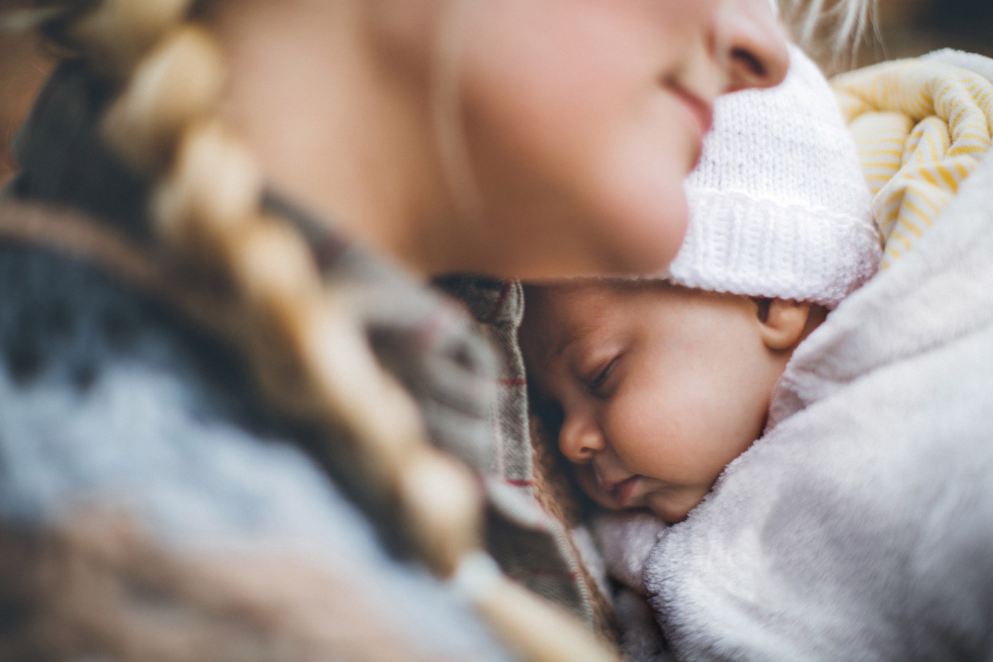 Mom snuggling a sleeping, bundled newborn baby